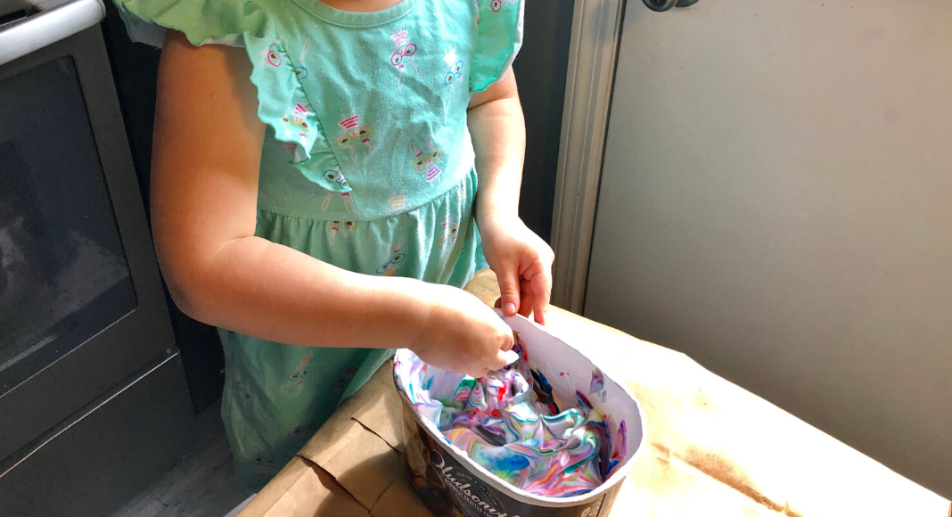 A child in a bunny dress swirling food coloring into whipped topping in an empty Hudsonville Ice Cream container
